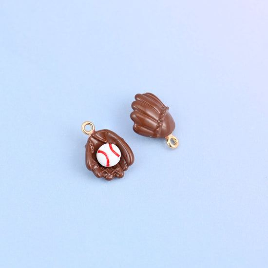 Two brown baseball glove charms, front and back, the ball sitting in the pocket with red stitching painted on.
