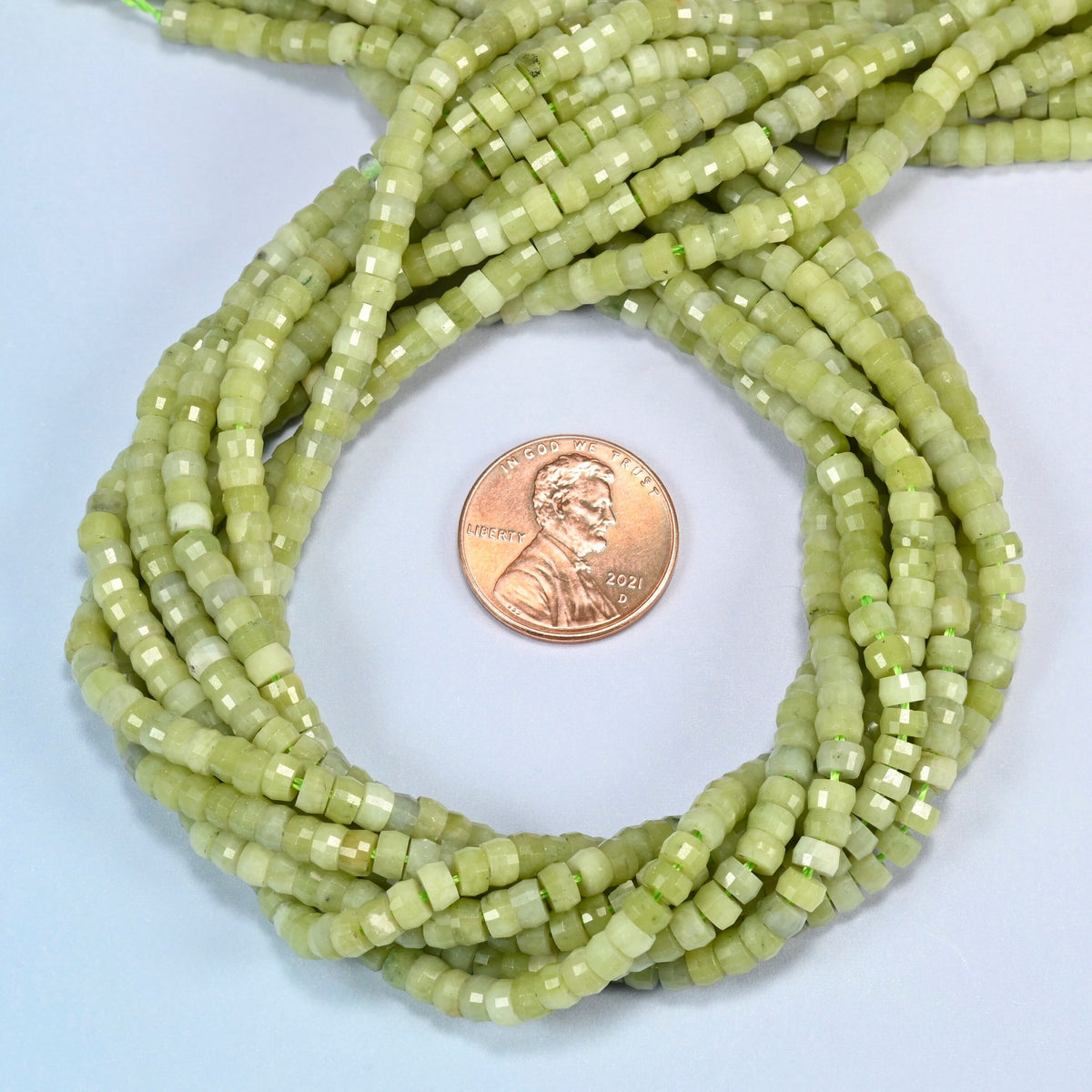 South Jade faceted heishi disc beads 2x4mm coiled in a loop around a US penny for scale, close-up of the faceted disc shape