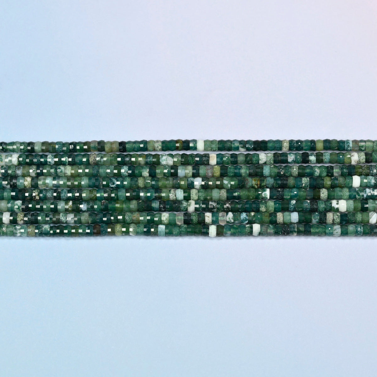 Several strands of moss agate faceted heishi disc beads laid in straight rows