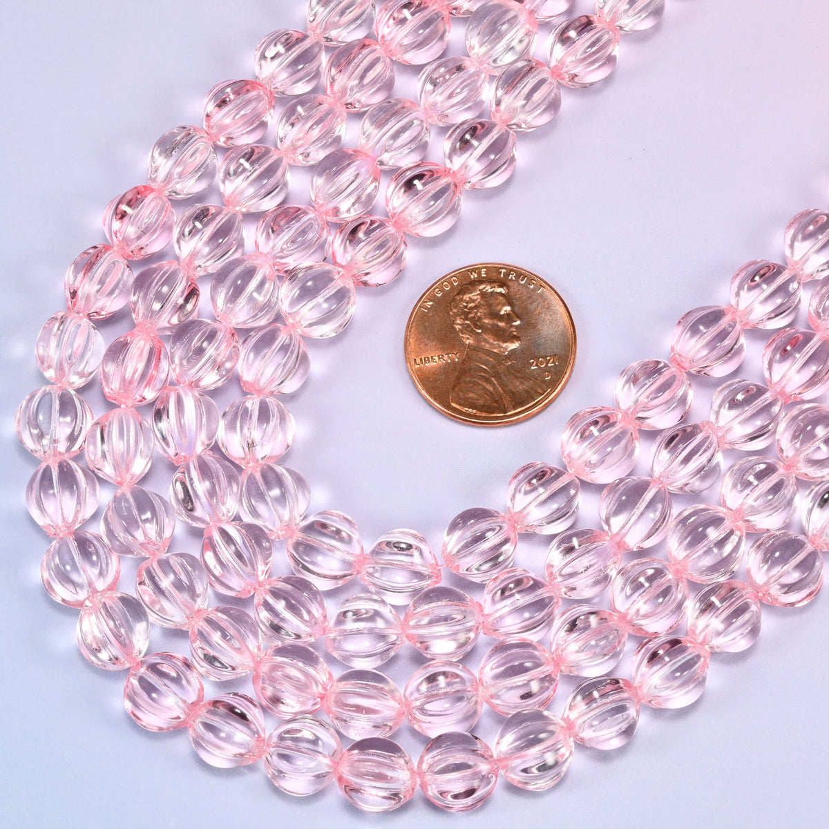 Clear pink pumpkin glass beads, 8mm melon rounds, strands laid in a gentle wave straight across the frame.