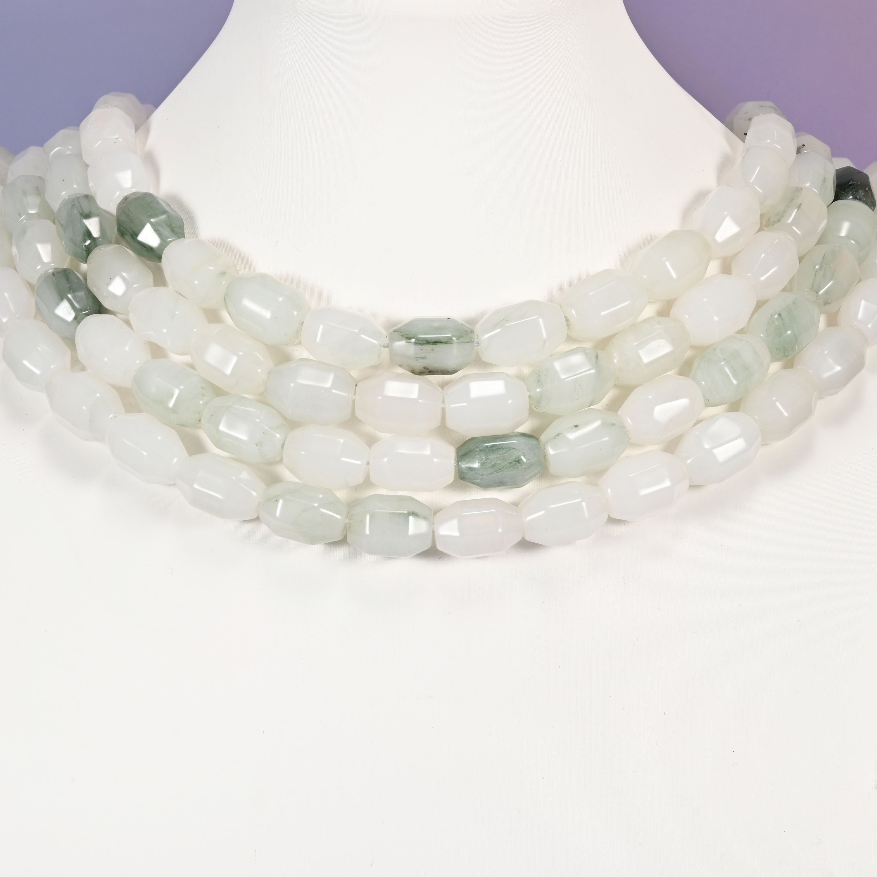 Multi-strand necklace of Tianshan Jade faceted barrel beads laid on a white mannequin neck form against a lavender background.