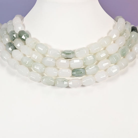Multi-strand necklace of Tianshan Jade faceted barrel beads laid on a white mannequin neck form against a lavender background.