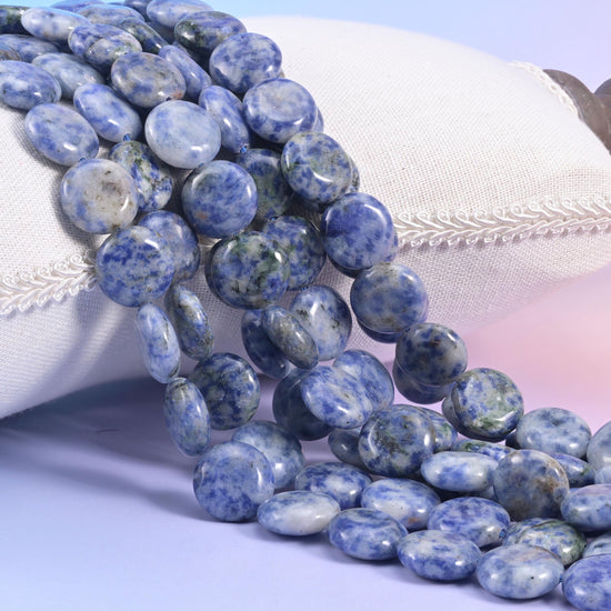Blue spot jasper coin strands resting on a cream cushion, pale grey discs speckled with powder blue