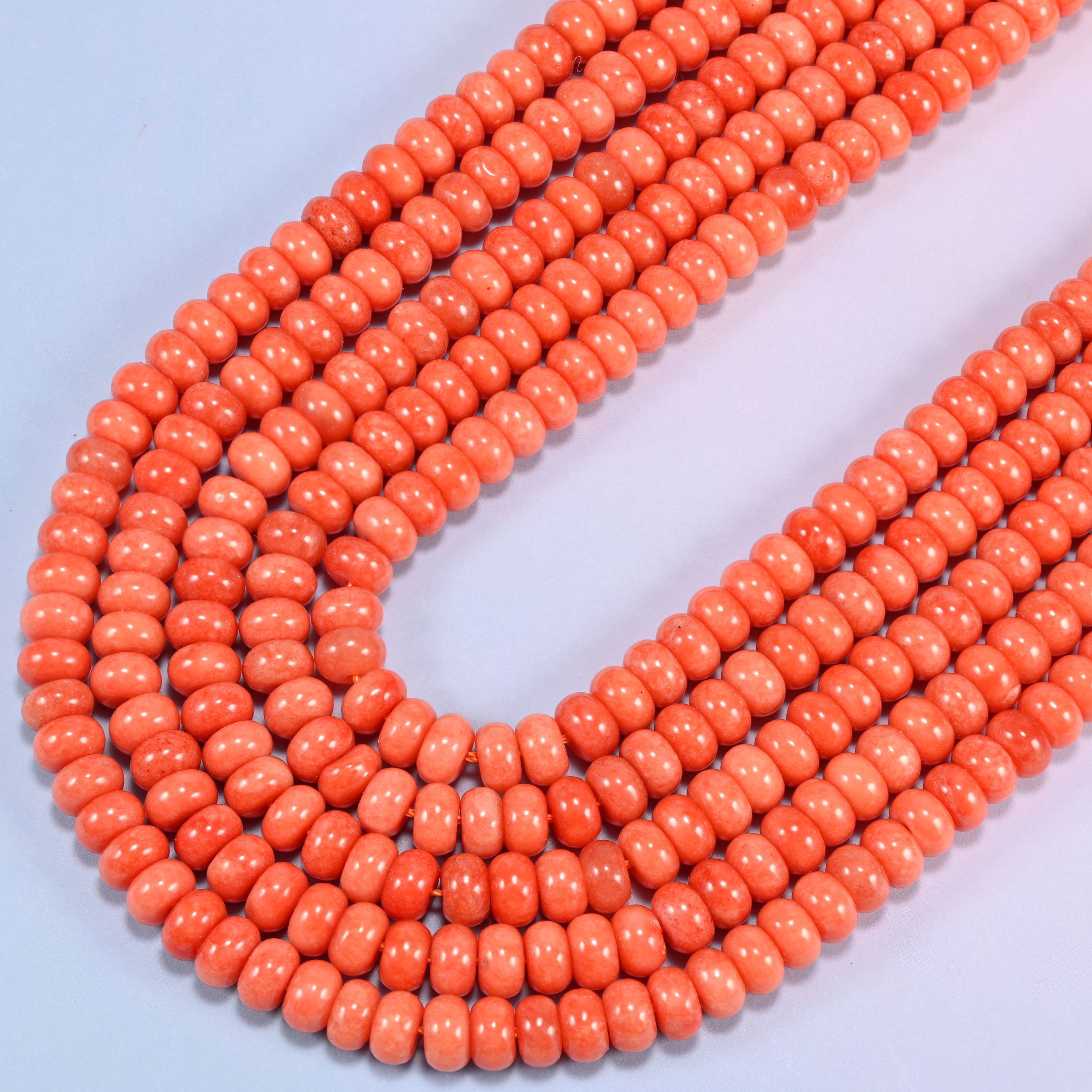 Red Orange dyed jade gemstone rondelle beads curving in a wide U across the frame, colour even from bead to bead