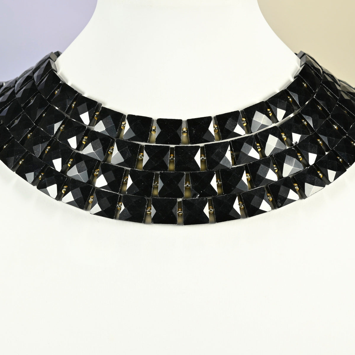 Natural black onyx faceted flat square strands arranged as a layered collar on a white display bust, black beads across the neck