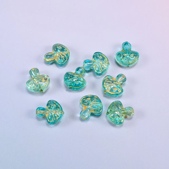 A scattered group of loose 13x12mm aqua gold flat mushroom glass beads, showing the gill lines under each cap.
