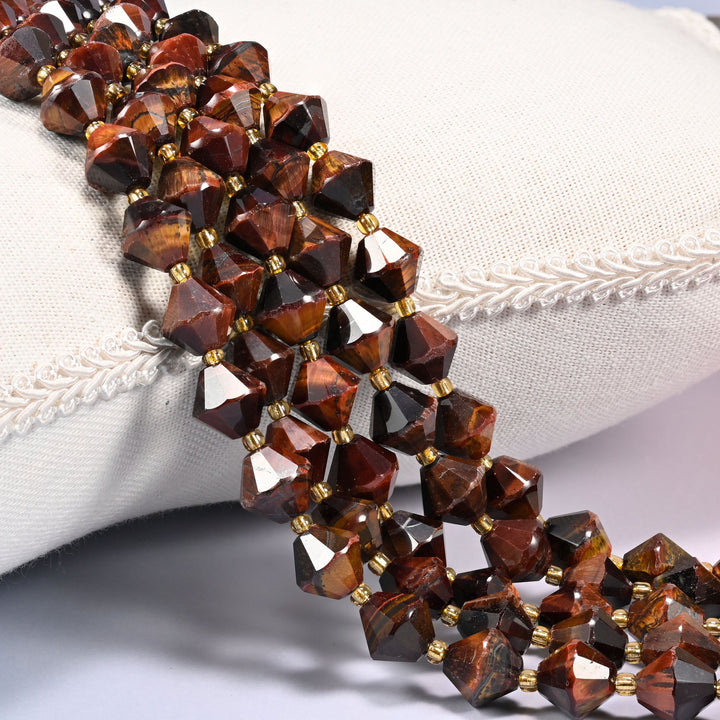 Red Tiger Eye faceted bicone beads draped over a cushion, close-up of the chatoyant banding and gold-tone spacers.