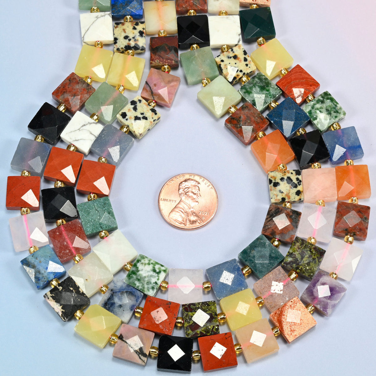 Assorted gemstone faceted flat square strands formed into a teardrop loop around a US penny for scale