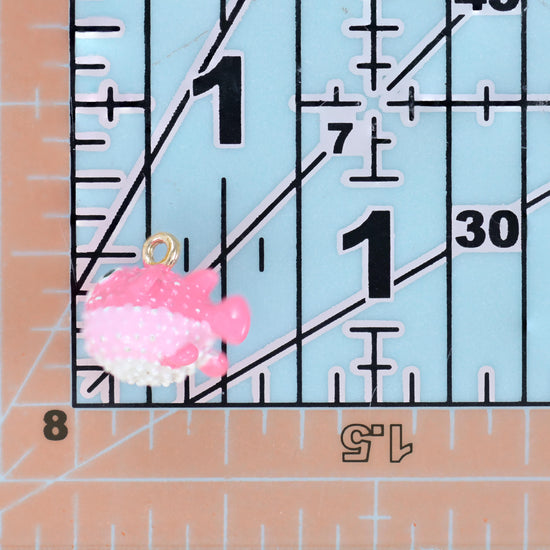 Enamel blowfish charm in pink on a quilting ruler, sitting just under the 1 inch mark for scale.