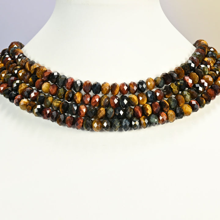 Tricolor tiger eye faceted rondelle strands arranged as a layered collar on a white display bust, gold, red and blue-gray beads across the neck