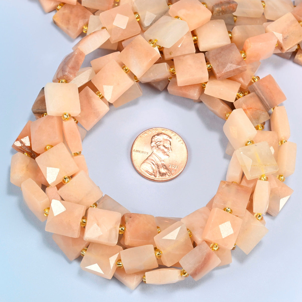 Natural pink aventurine faceted flat square beads 10x10mm coiled in a loop around a US penny for scale, close-up of the faceted flat square shape