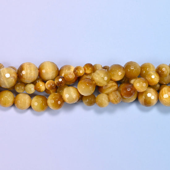 Gold tiger eye faceted round beads with a soft silky sheen across wheat gold and caramel banding, lighter and creamier than standard brown tiger eye.