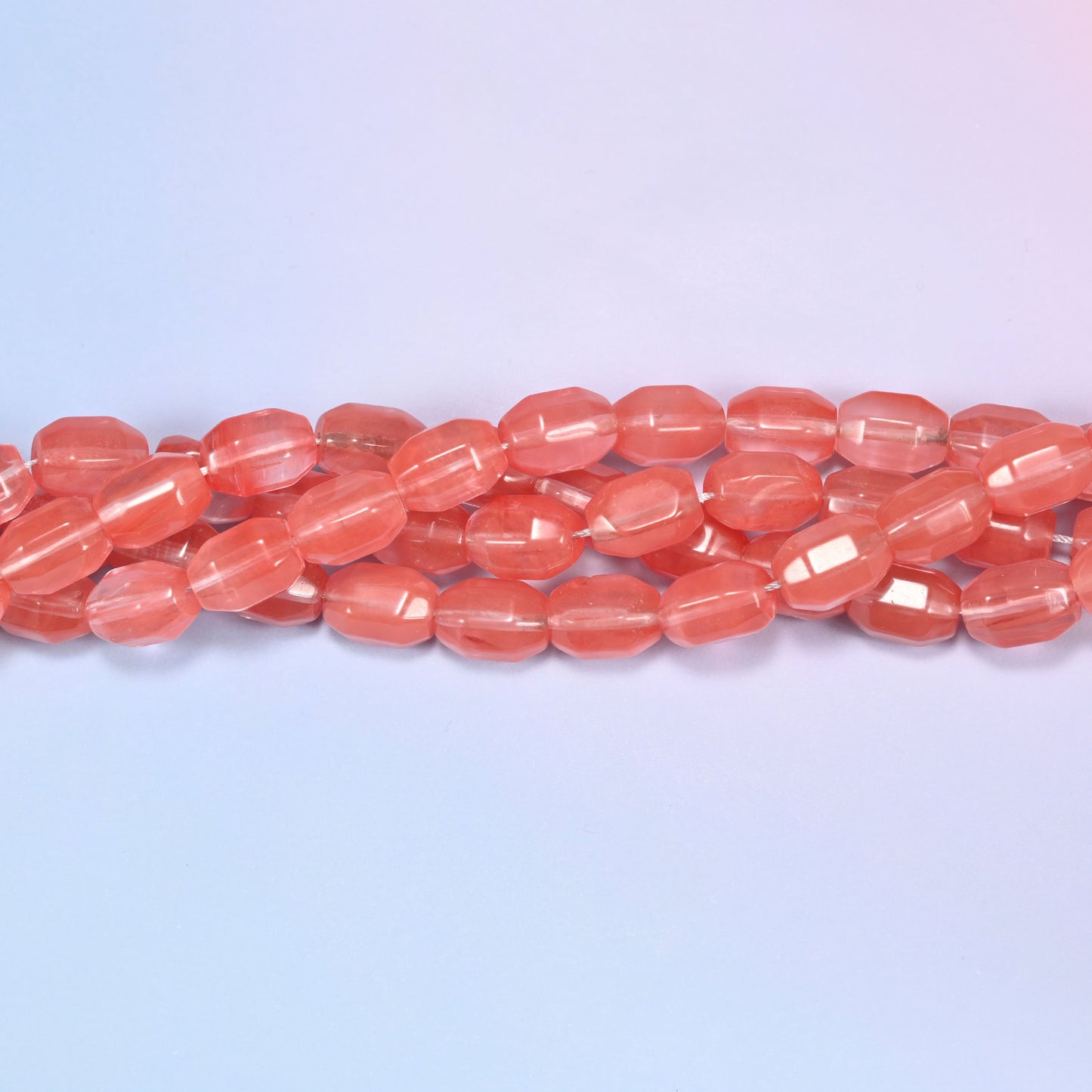 Close-up horizontal row of coral pink faceted glass barrel beads laid straight, showing the polished facet detail and translucency.
