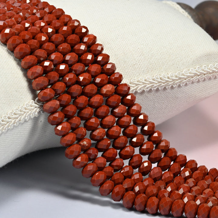 Dark red jasper faceted rondelle beads 5x8mm in deep brick red, several strands draped over a white cushion