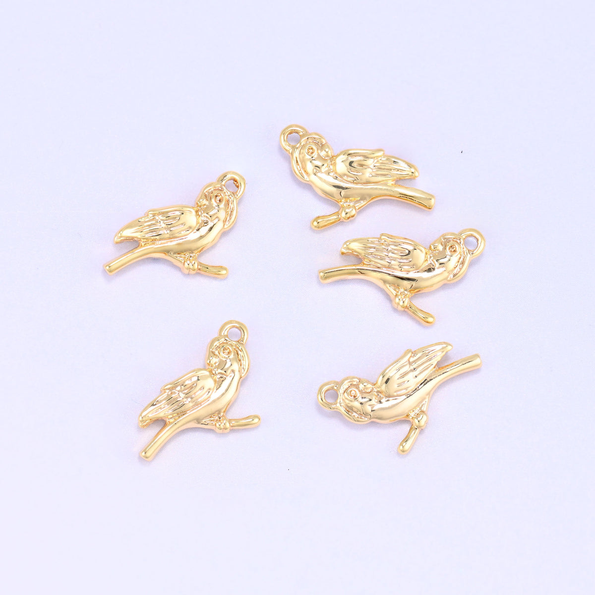 Small gold charms bird, five 18K gold plated bird charms grouped on a lilac backdrop