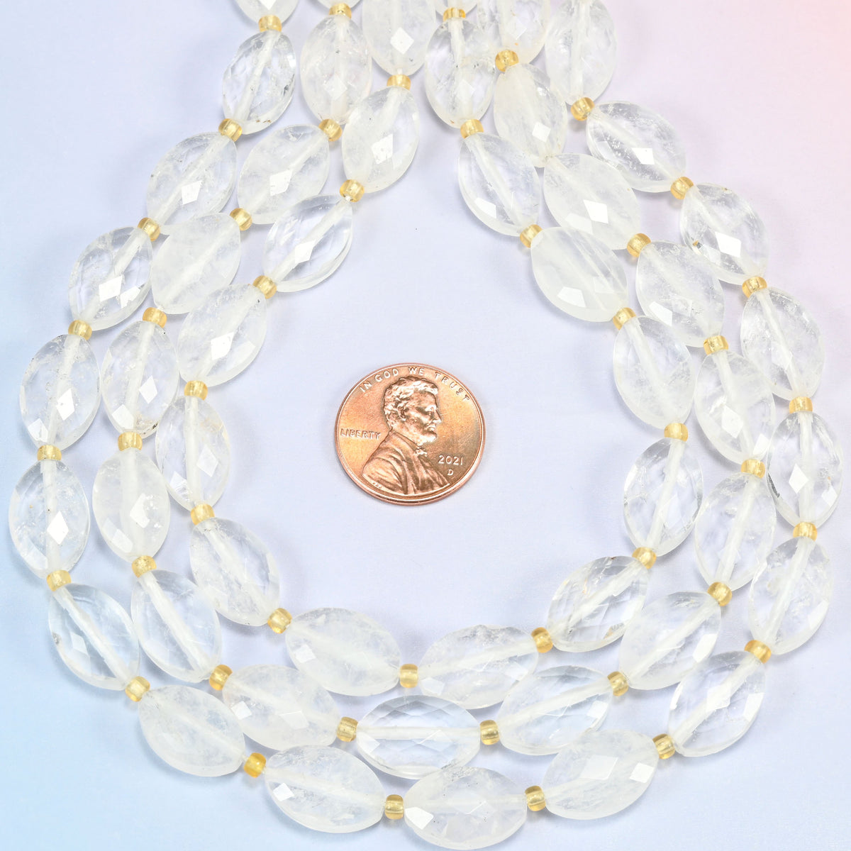 Clear quartz faceted flat oval strands formed into a teardrop loop around a US penny for scale