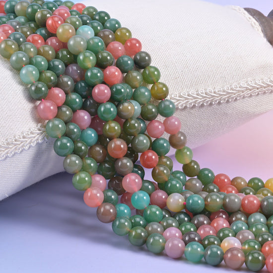 Green Yanyuan Agate smooth round beads, strands draped over a white cushion, sage green mixed with coral pink, aqua and cream