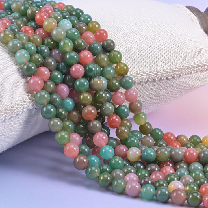 Green Yanyuan Agate smooth round beads, strands draped over a white cushion, sage green mixed with coral pink, aqua and cream