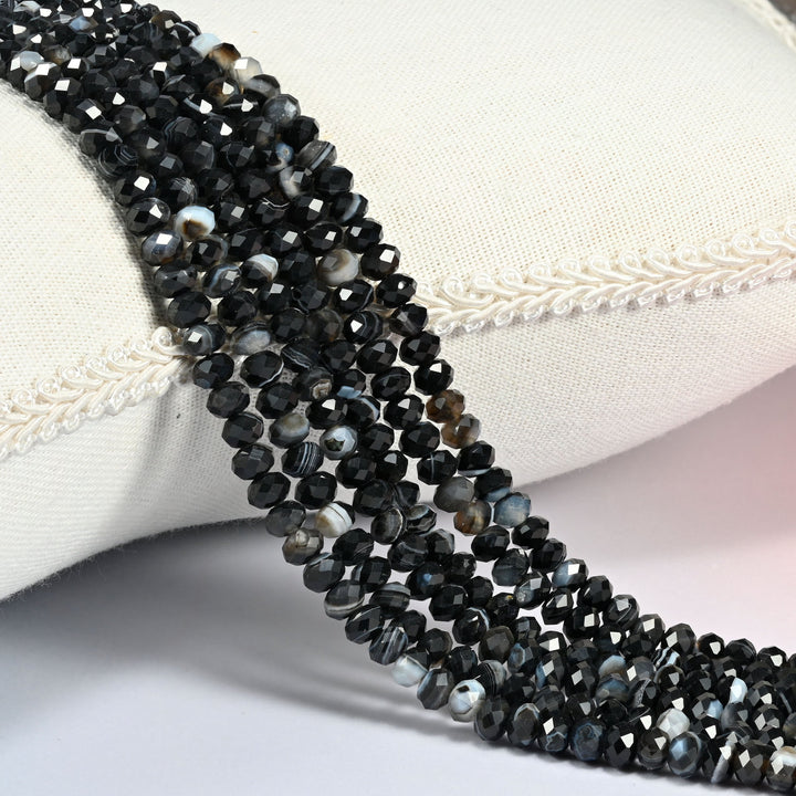 Dyed Black Strip Agate gemstone rondelle beads 4x6mm faceted, strand draped over a cream fabric cushion