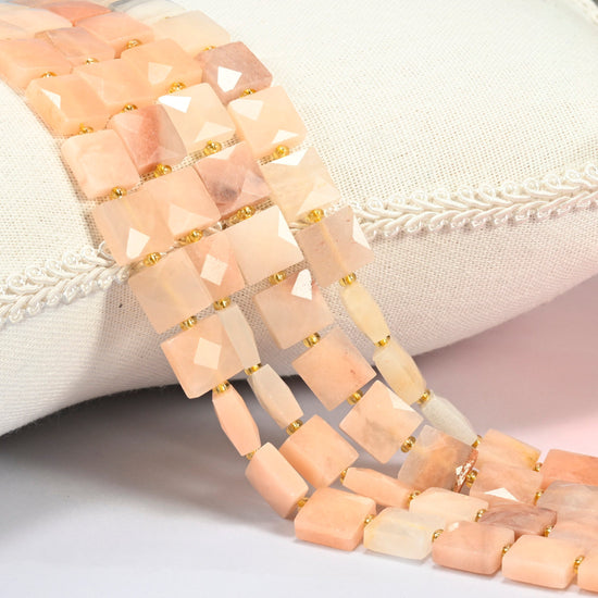 Natural pink aventurine faceted flat square beads 10x10mm with small gold seed bead spacers, several strands draped over a white cushion
