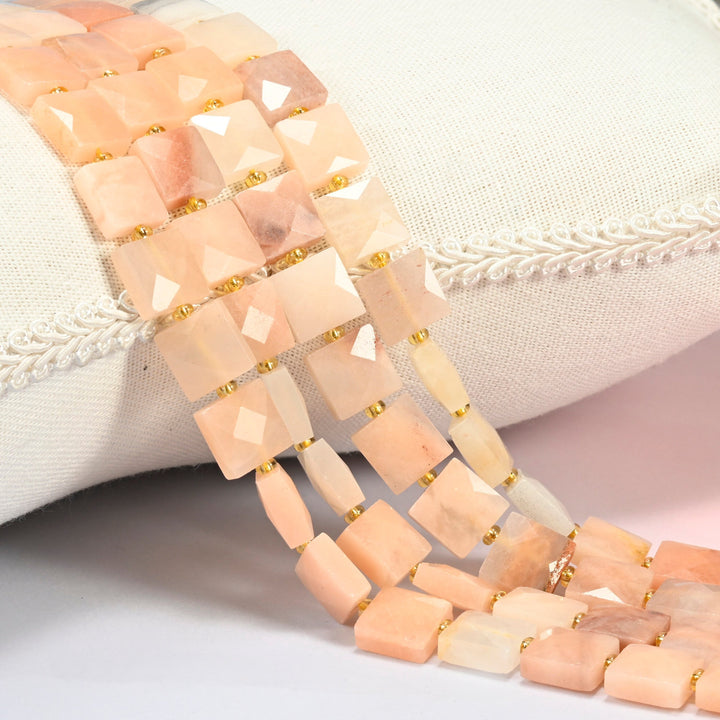 Natural pink aventurine faceted flat square beads 10x10mm with small gold seed bead spacers, several strands draped over a white cushion