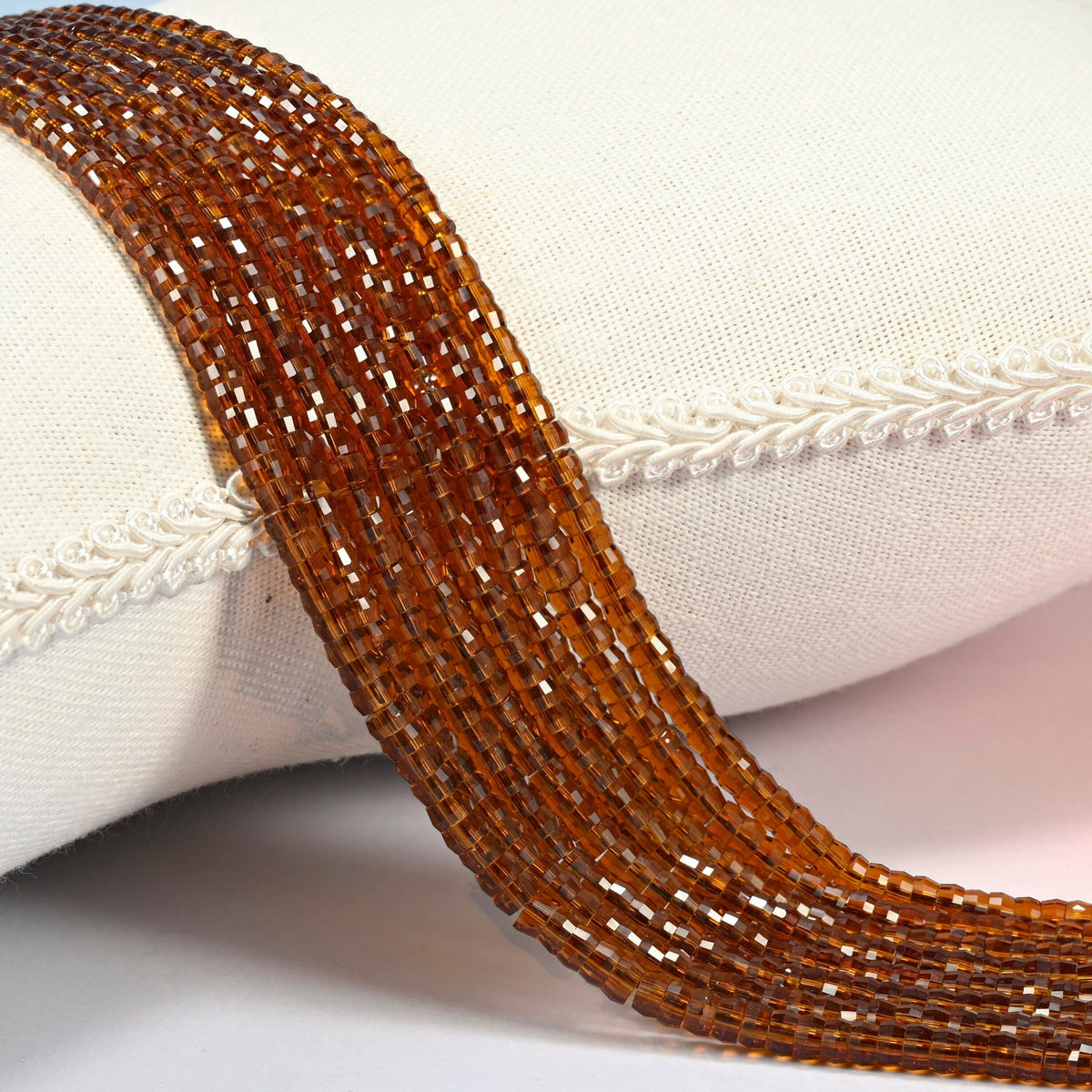 Brown glass faceted heishi disc beads 2x4mm, several strands draped over a white cushion