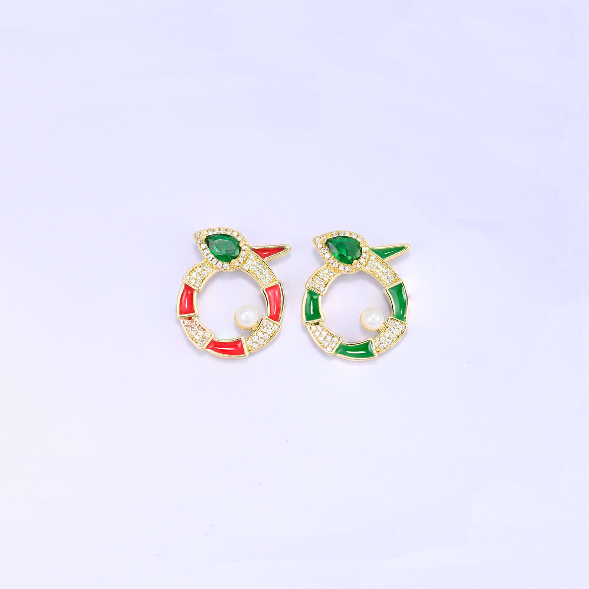 Round snake charm colourways side by side, the red enamel version and the green enamel version, each gold plated with a green pear cut stone and a small pearl.