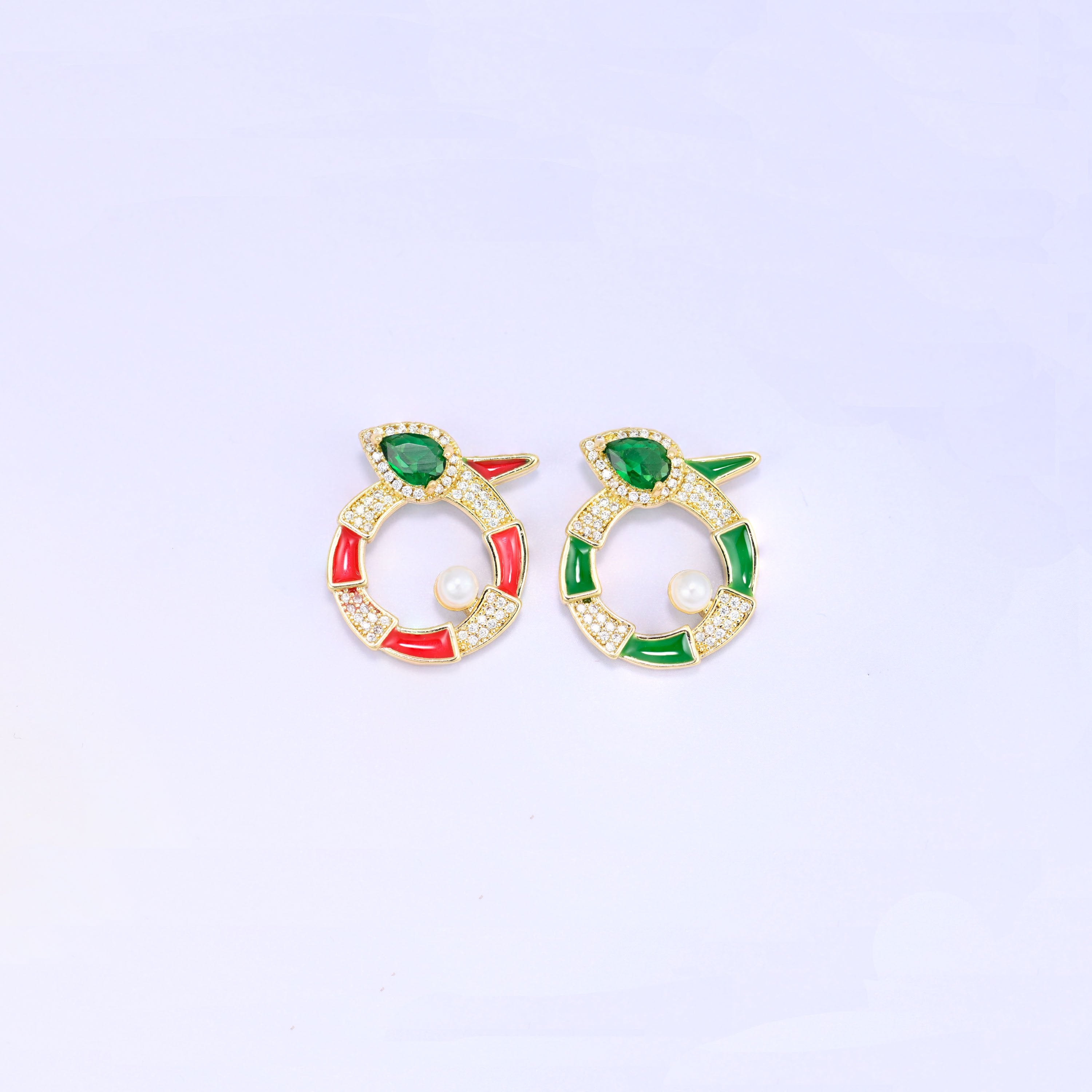 Round snake charm colourways side by side, the red enamel version and the green enamel version, each gold plated with a green pear cut stone and a small pearl.