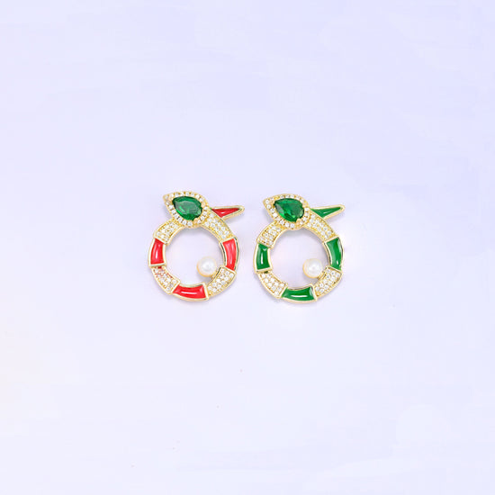 Round snake charm colourways side by side, the red enamel version and the green enamel version, each gold plated with a green pear cut stone and a small pearl.