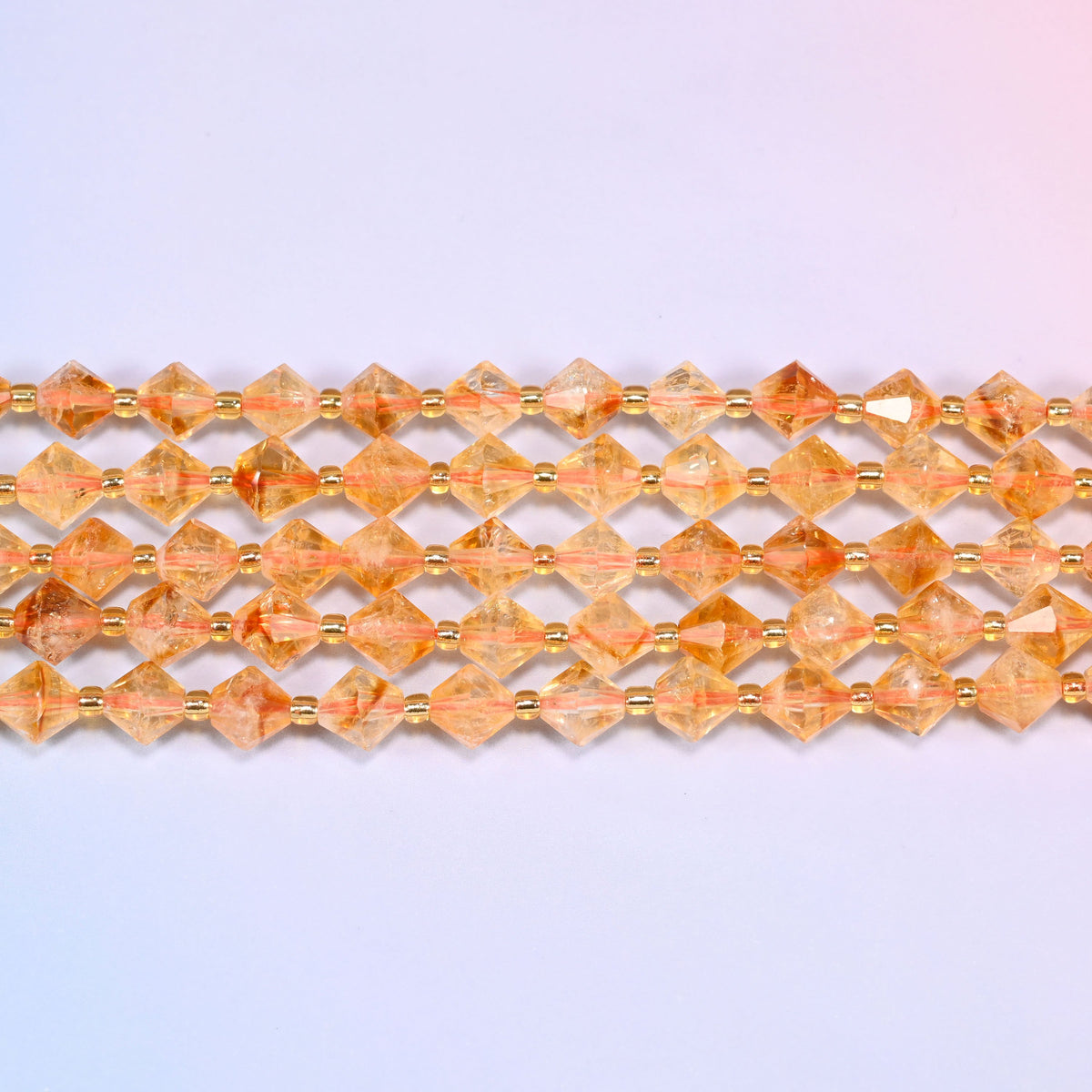 Citrine bicone beads in straight rows, seen close up, each bead cut to two points meeting at a wide center.