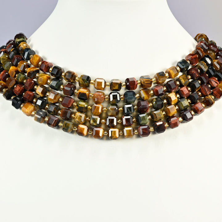 Tricolor tiger eye faceted cube strands arranged as a layered collar on a white display bust, gold, red and blue-gray beads across the neck