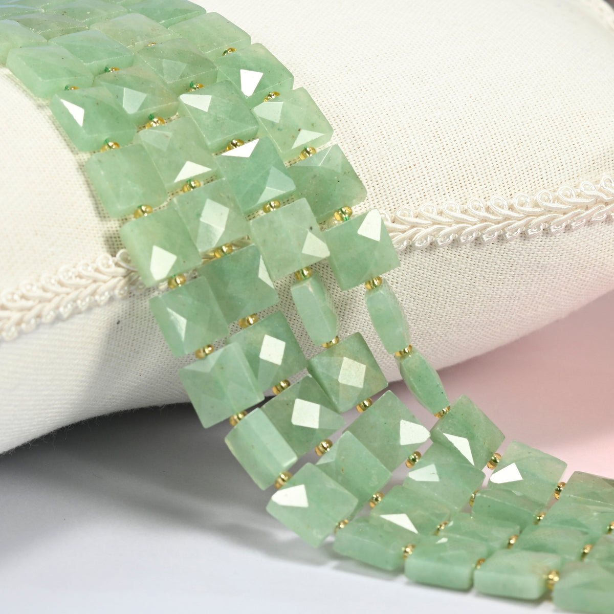 Natural green aventurine faceted flat square beads 10x10mm with small gold seed bead spacers, several strands draped over a white cushion