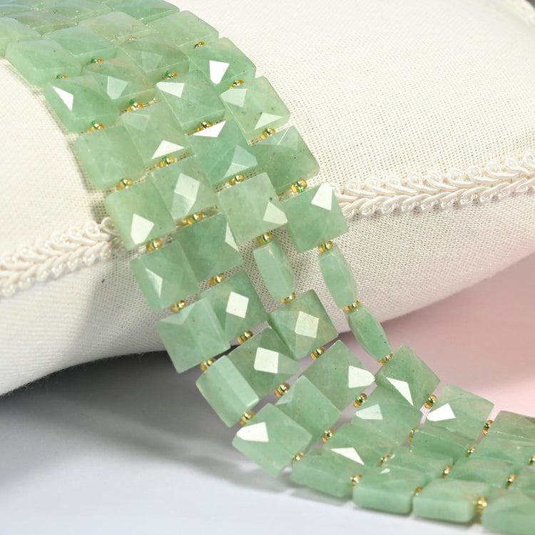 Natural green aventurine faceted flat square beads 10x10mm with small gold seed bead spacers, several strands draped over a white cushion