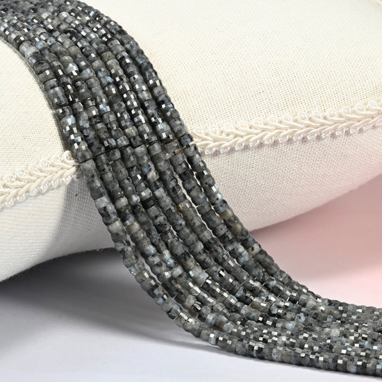 Black labradorite faceted heishi disc beads 2x4mm, several strands draped over a white cushion