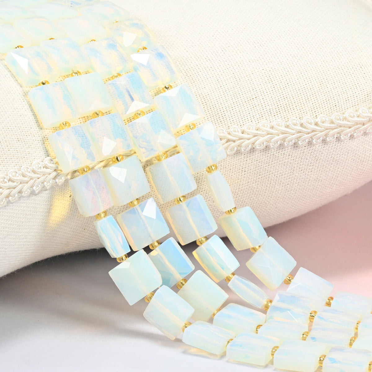Opalite faceted flat square beads 10x10mm with small gold seed bead spacers, several strands draped over a white cushion
