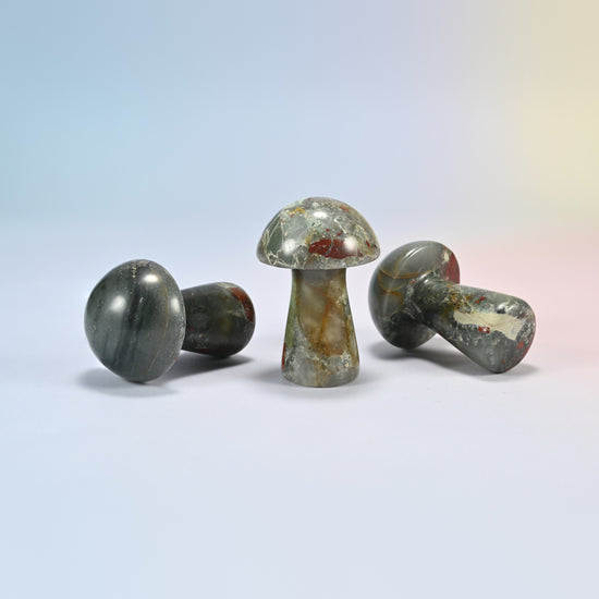 Three 2 inch African bloodstone mushroom crystal carvings shown standing and lying, gray-green with red and tan patches