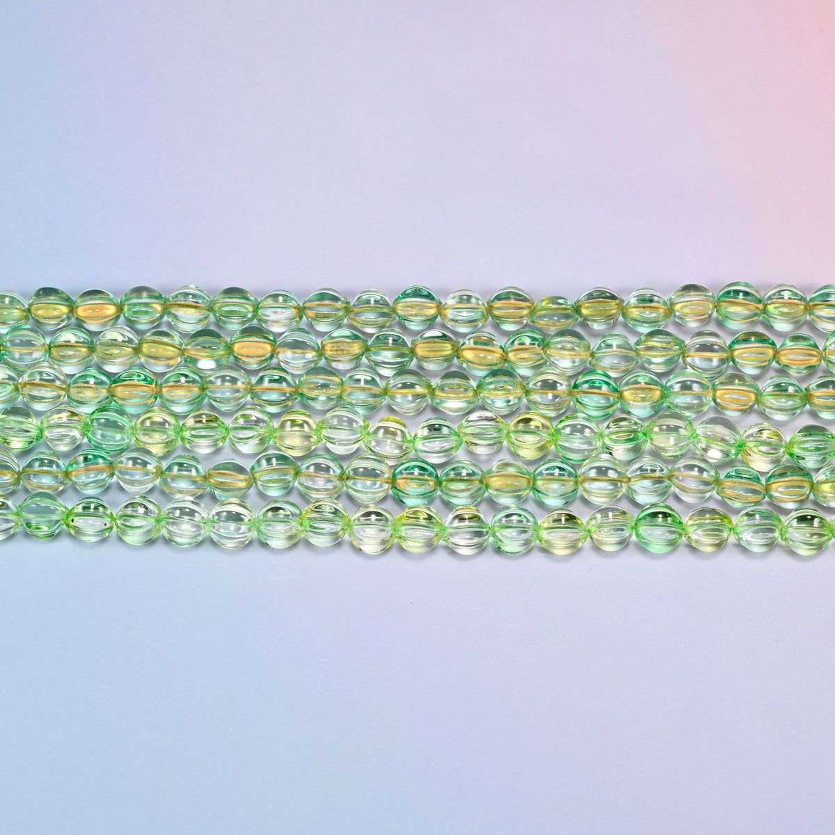 Close-up of 8mm green gold pumpkin glass beads in four horizontal rows, showing the carved melon ribs.