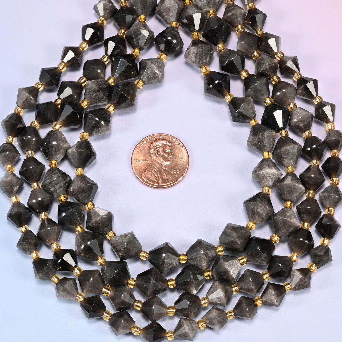 Silver obsidian bicone beads coiled into a ring, seen from above, the sheen strongest on the upper facets.