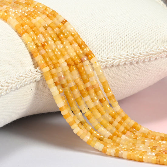Gold Silk Jade faceted heishi disc beads 2x4mm, several strands draped over a white cushion