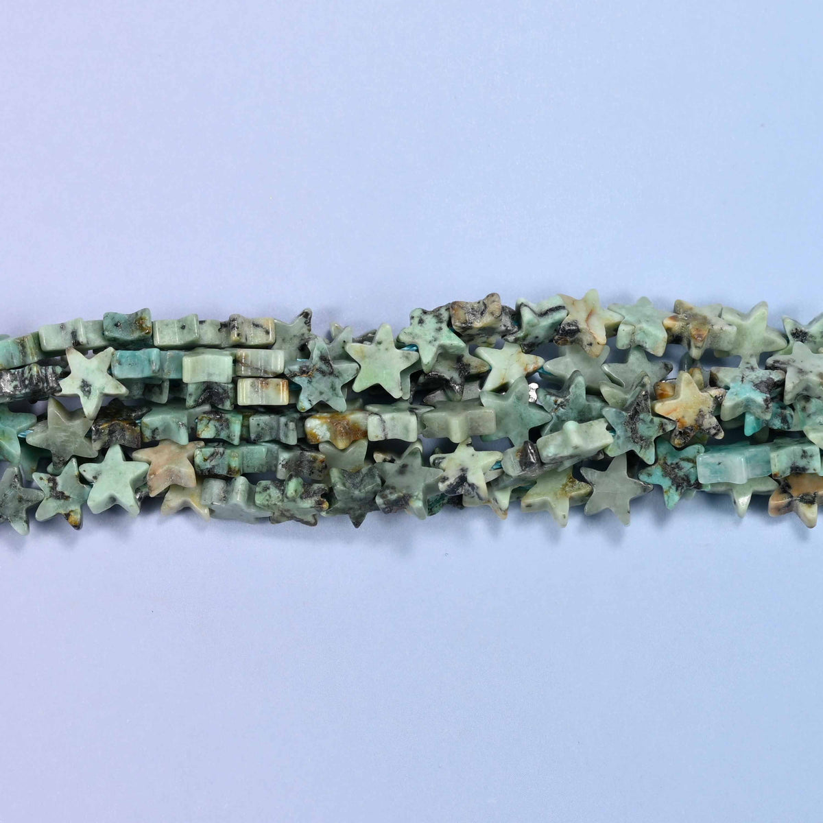 Small five-pointed stars in soft sage and celadon green, veined with dark green-black matrix and the odd warm tan fleck, polished flat on both faces.