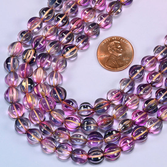 Pink blue gold pumpkin glass beads laid in a wide shallow bend, pink and blue-violet running together through the glass with a warm gold stripe down each rib.