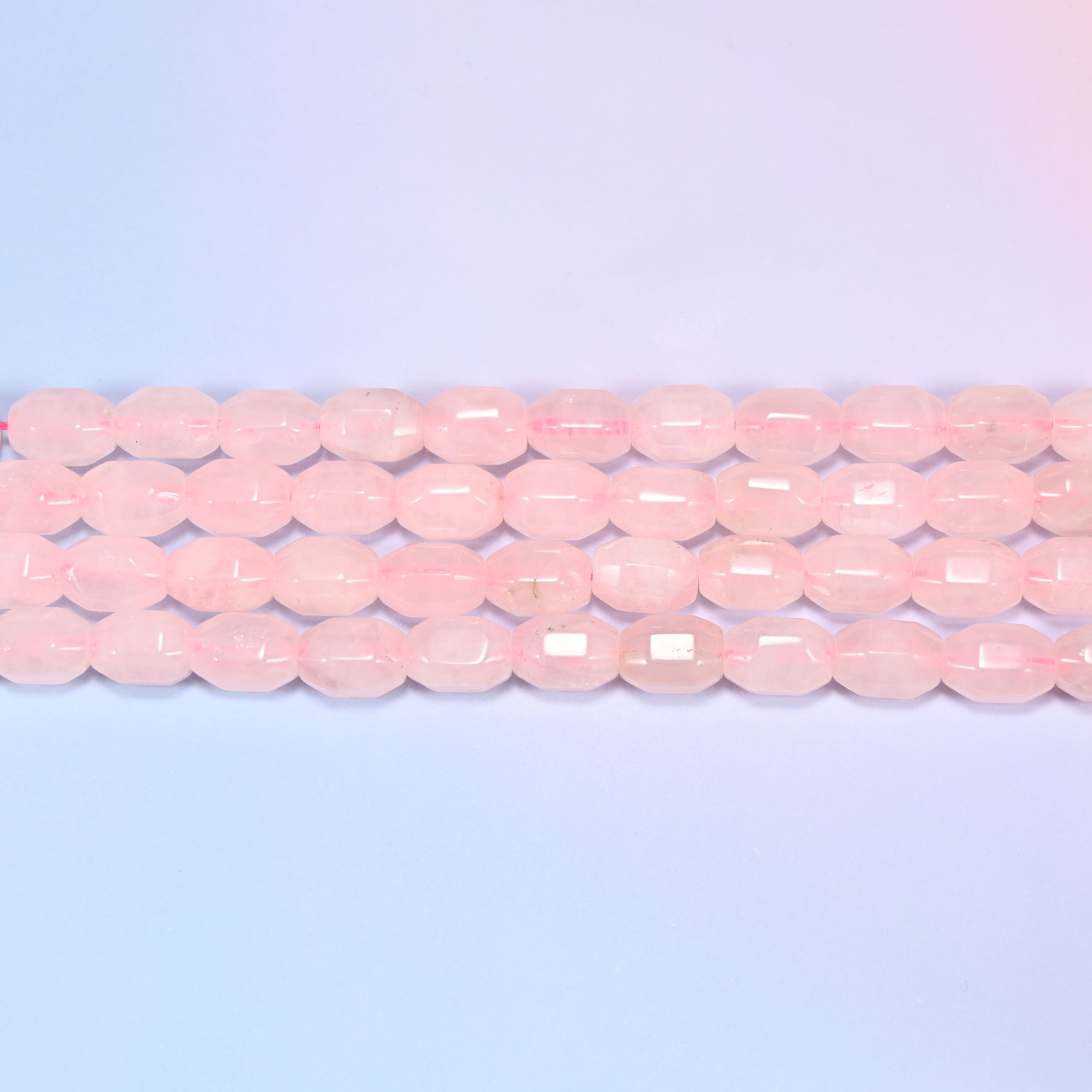 Close-up rows of Rose Quartz faceted barrel beads laid diagonally, showing the soft blush pink tone and facet cuts.