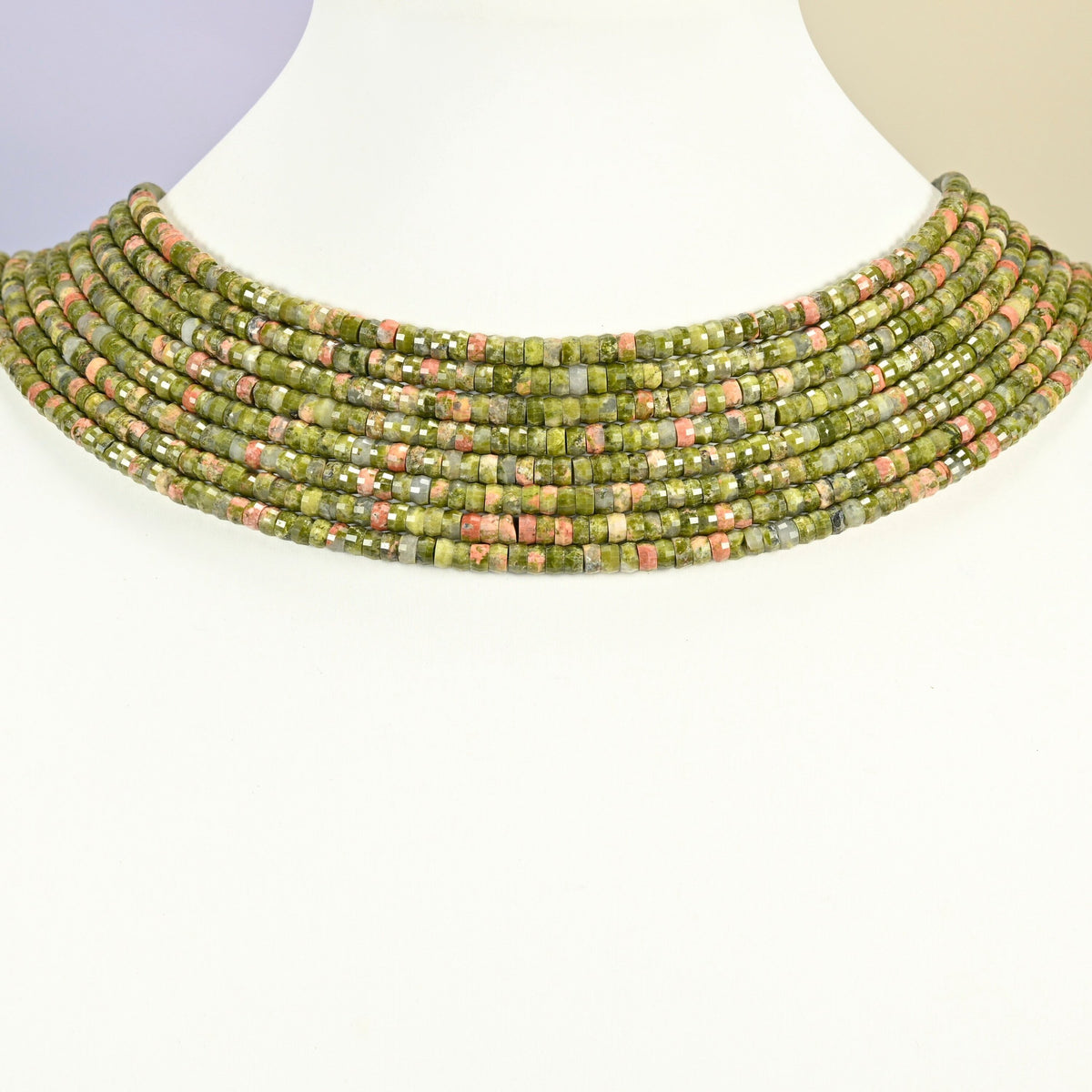 Unakite faceted heishi disc strands arranged as a layered collar on a white display bust, green and pink beads across the neck