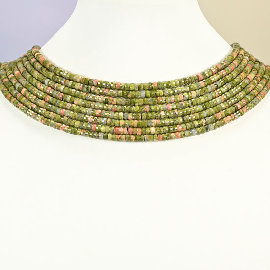 Unakite faceted heishi disc strands arranged as a layered collar on a white display bust, green and pink beads across the neck