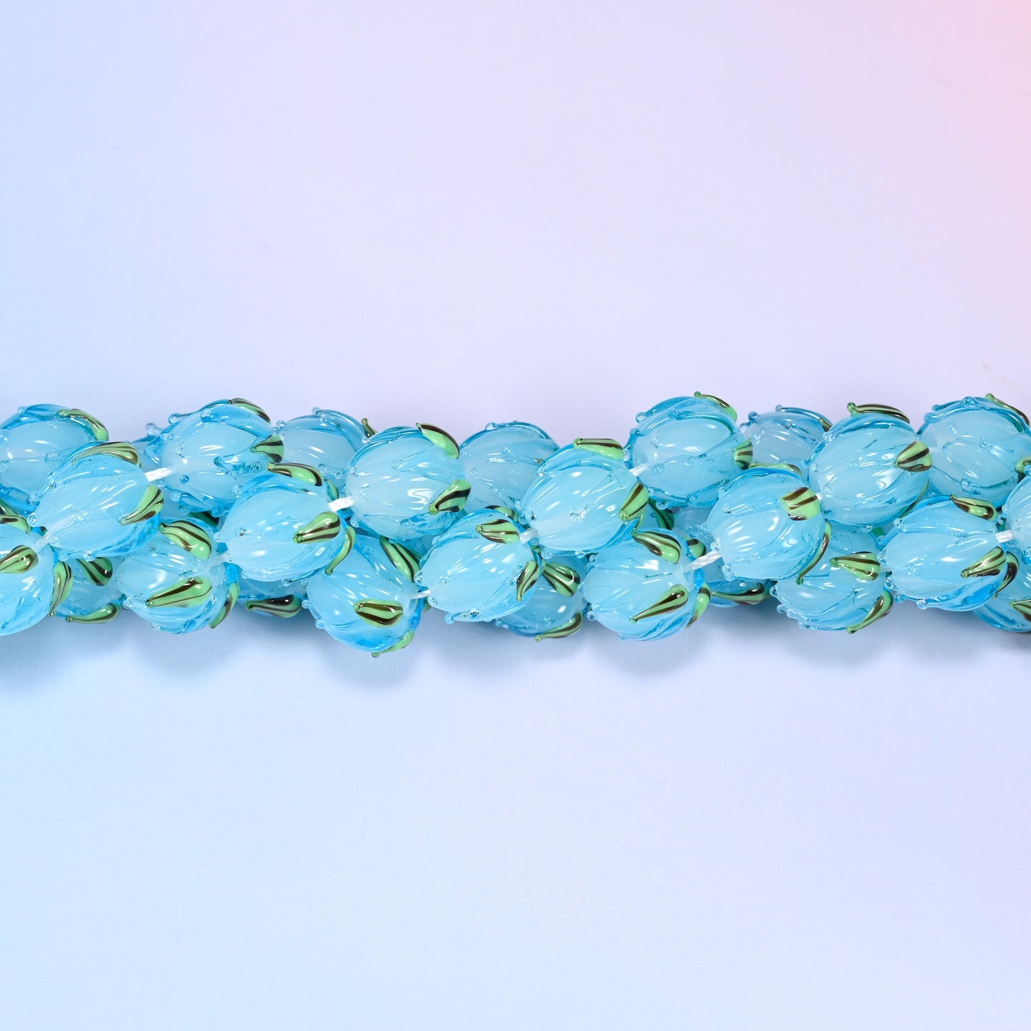 Sky blue tulip bud-shaped lampwork glass beads, translucent glass with hand-formed sculpted petal detailing that gives a realistic flower bud look, accented with a green leaf detail at the base.
