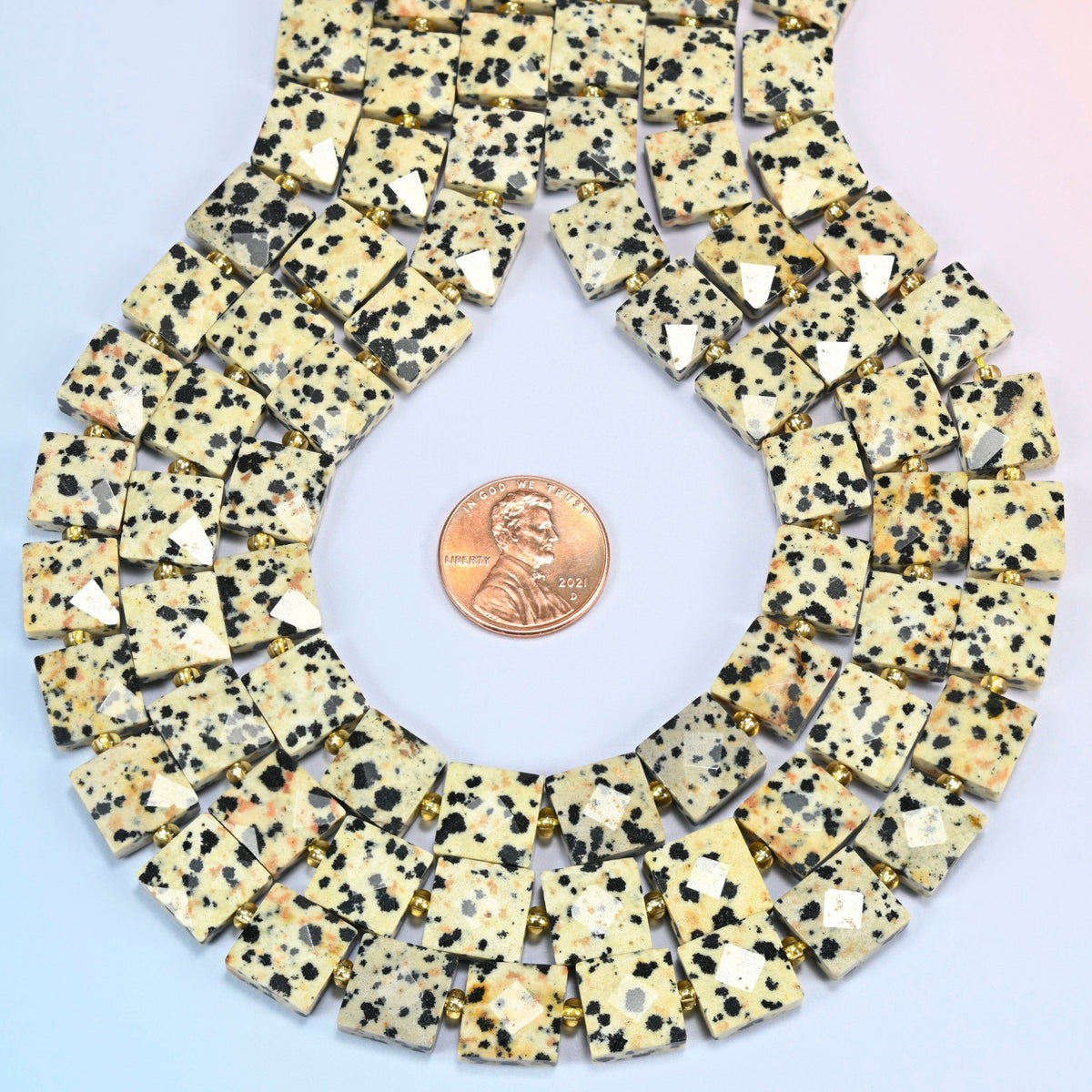 Dalmatian jasper faceted flat square strands formed into a teardrop loop around a US penny for scale