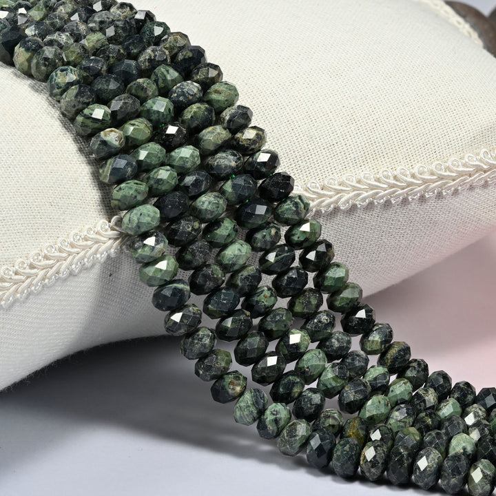 Kambaba jasper faceted rondelle beads 5x8mm in deep forest green with sage orbs, several strands draped over a white cushion