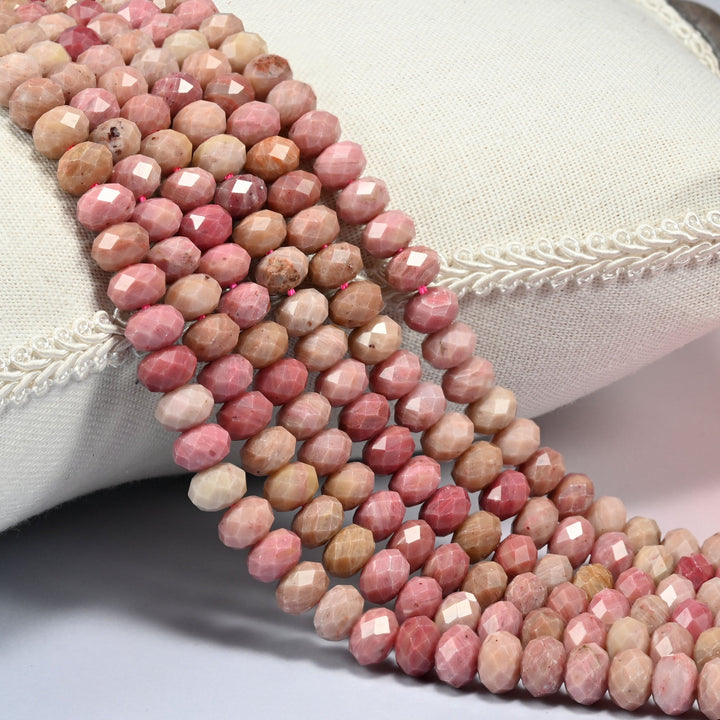 Pink rhodonite faceted rondelle beads in soft rose and salmon pink mottled with cream and light tan, three strands draped over a linen cushion