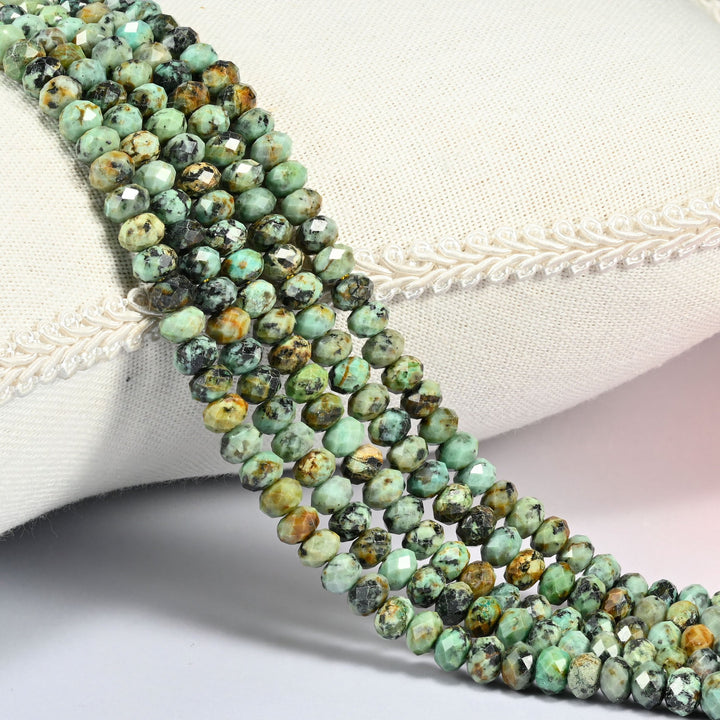 African Howlite gemstone rondelle beads 4x6mm faceted, strand draped over a cream fabric cushion