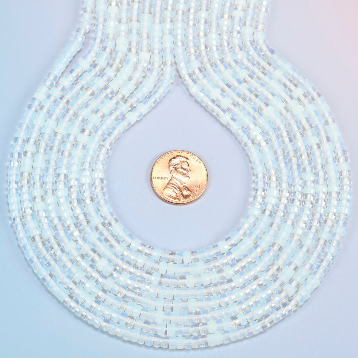 Opalite faceted heishi disc strands formed into a teardrop loop around a US penny for scale